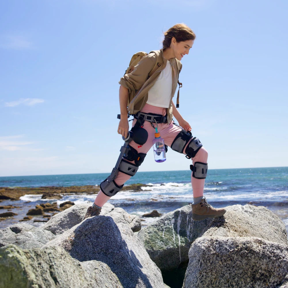 A woman is walking on rocks wearing the Ascentiz knee exoskeleton