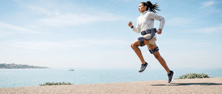 A runner wearing an Ascentiz hip exoskeleton on a sunny coastal path.