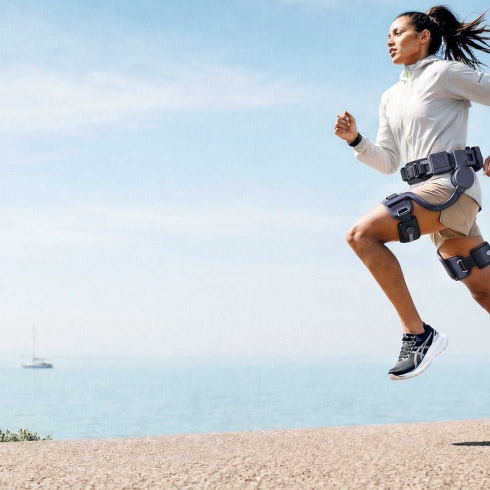 A runner wearing an Ascentiz hip exoskeleton on a sunny coastal path.
