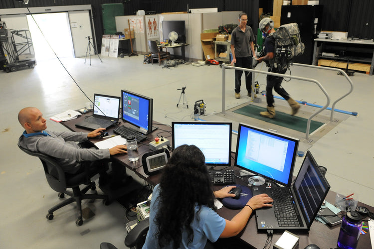 Soldier walking on a treadmill while researchers evaluate a real soft exosuit