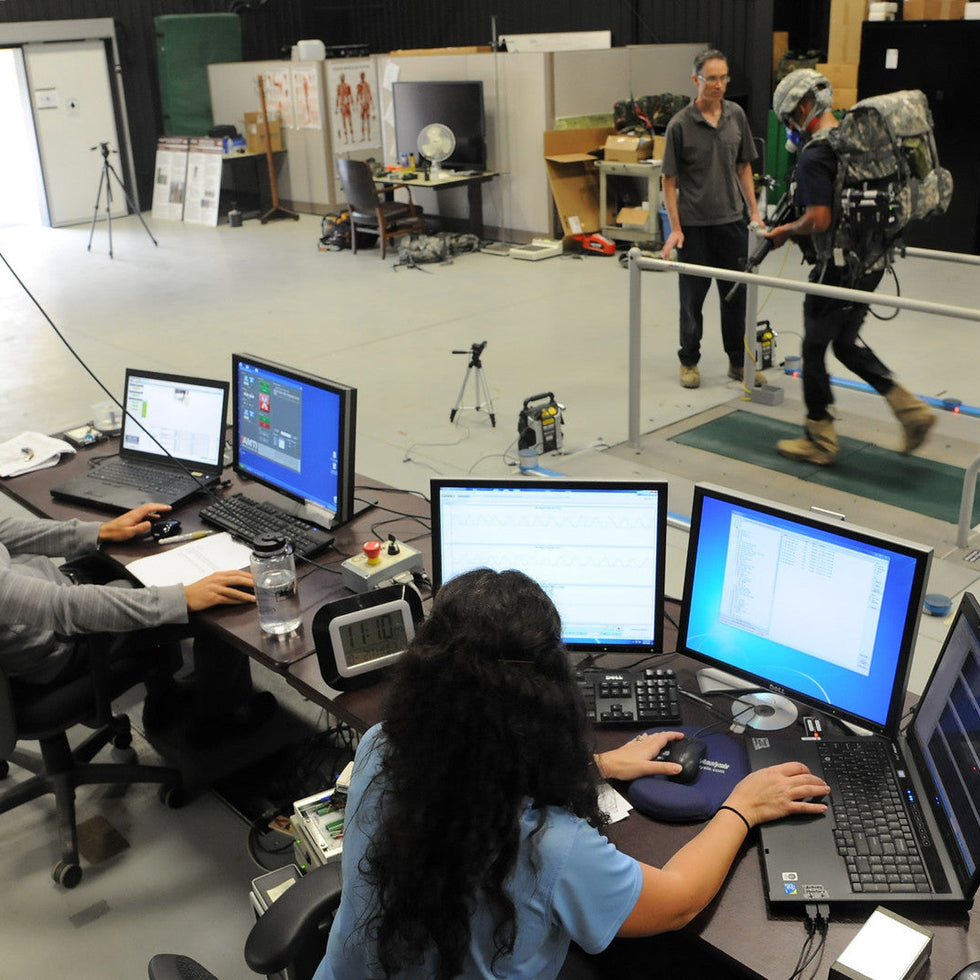 Soldier walking on a treadmill while researchers evaluate a real soft exosuit