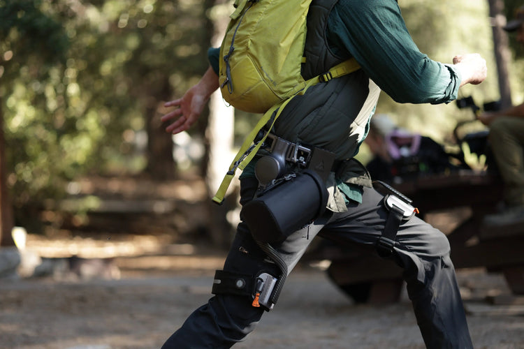 A hiker wears an Ascentiz hip exoskeleton with a backpack outdoors.