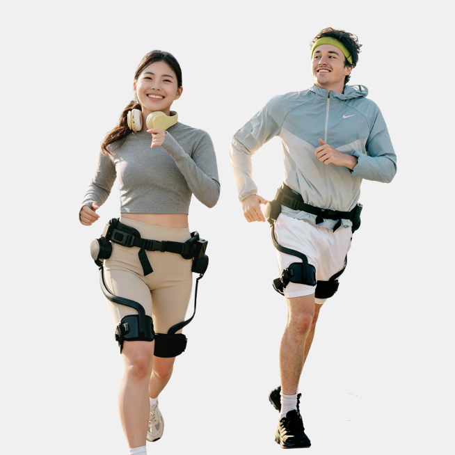 Mobile studio product shot of a female runner wearing the Ascentiz H Pro hip exoskeleton and a male runner wearing the Ascentiz Boost knee exoskeleton, derived from an outdoor photo, demonstrating runnable mobility technology on a clean background.