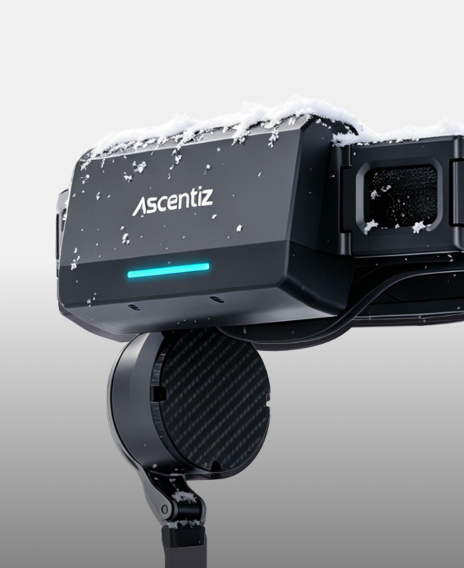 A close-up of the Ascentiz exoskeleton battery module with a glowing cyan LED, covered in snow to demonstrate reliable power performance in extreme winter weather. Vertical mobile view.