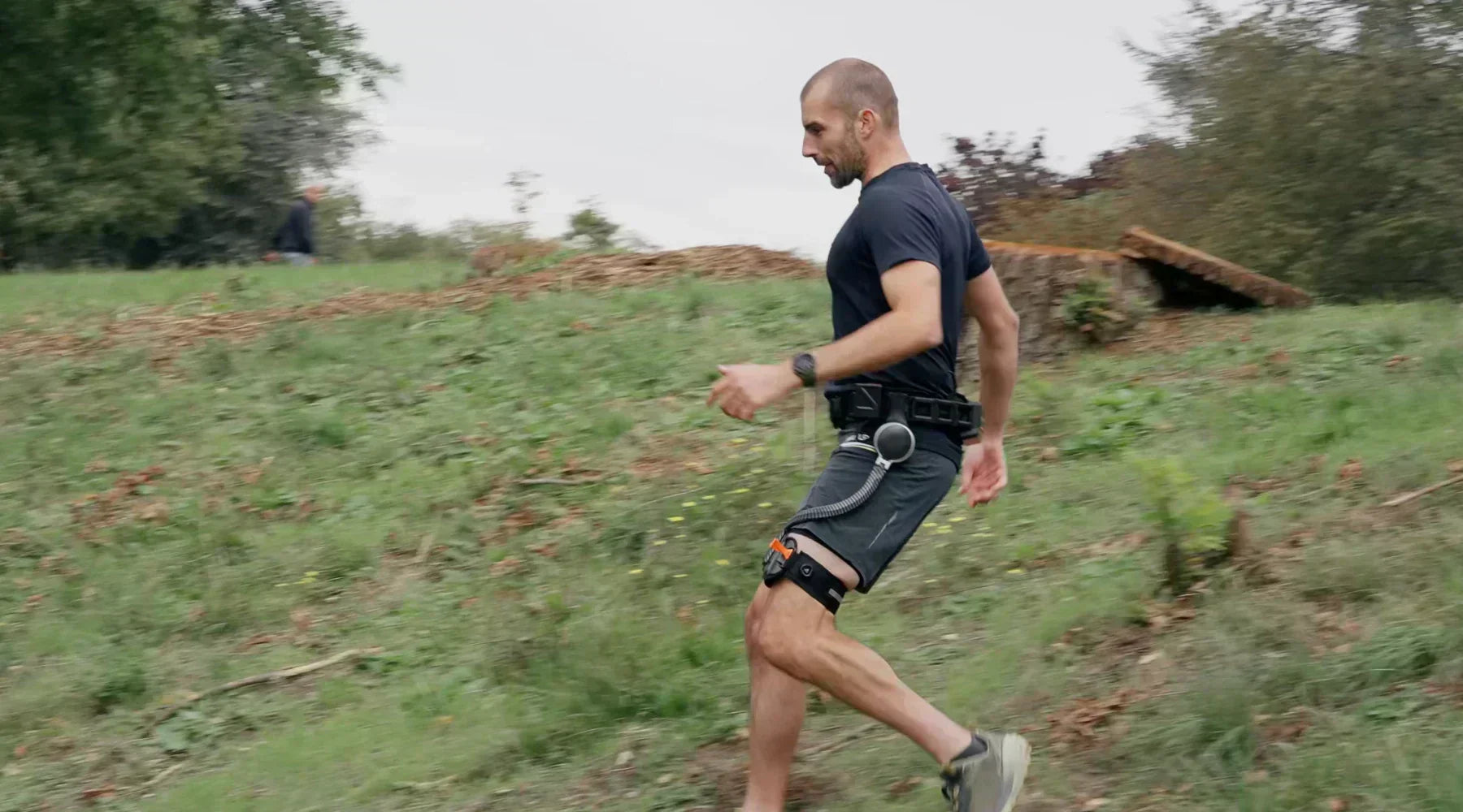 Blog lifestyle image of a male runner wearing the Ascentiz H hip exoskeleton while descending a grassy hill trail, showcasing downhill power assistance and reduced muscle fatigue.