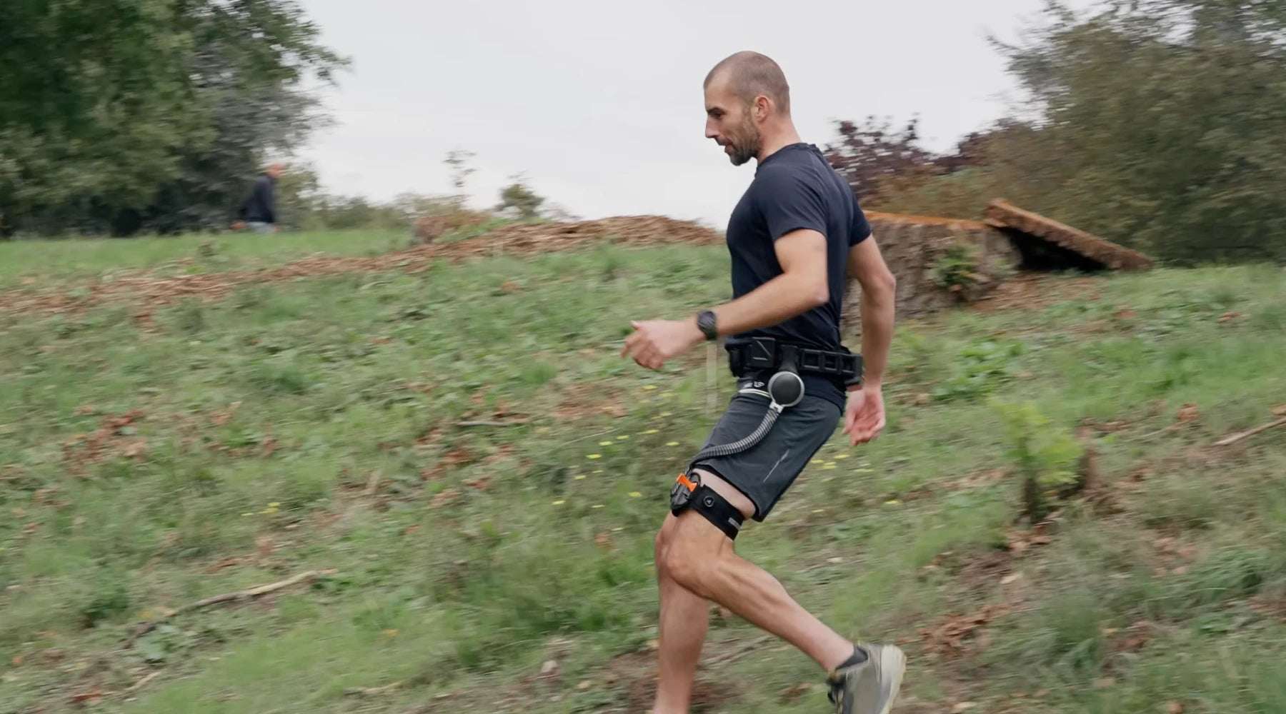 Website theme lifestyle image of a male runner wearing the Ascentiz H hip exoskeleton while descending a grassy hill trail, showcasing downhill power assistance and reduced muscle fatigue.