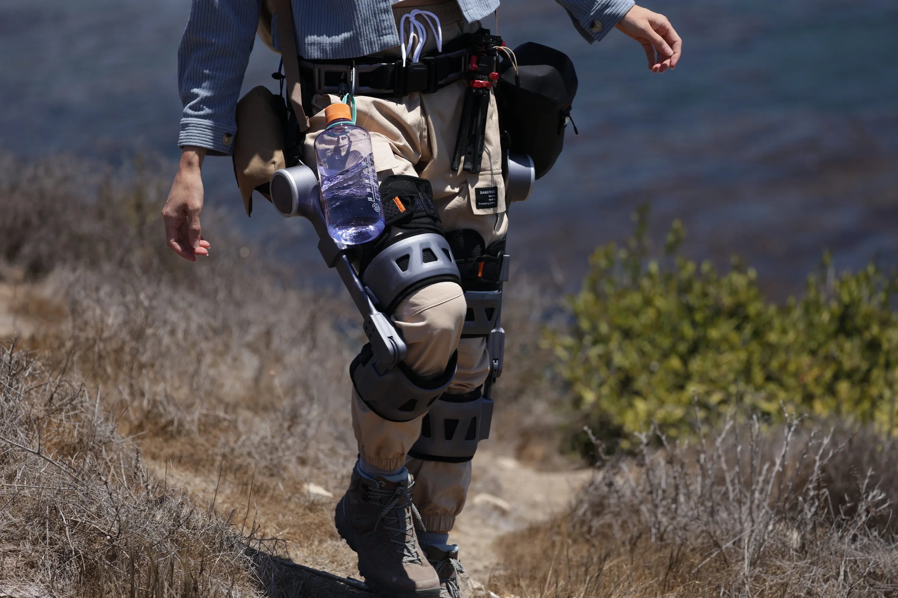 Woman walking lightly wearing Ascentiz K-module exoskeleton with water bottle and other outdoor gears on expandable belt