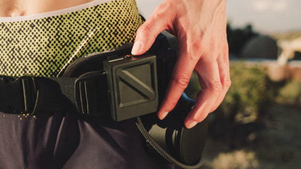 Close-up of a user's hand operating the square control module on the Ascentiz Exo-Belt Pro outdoors.