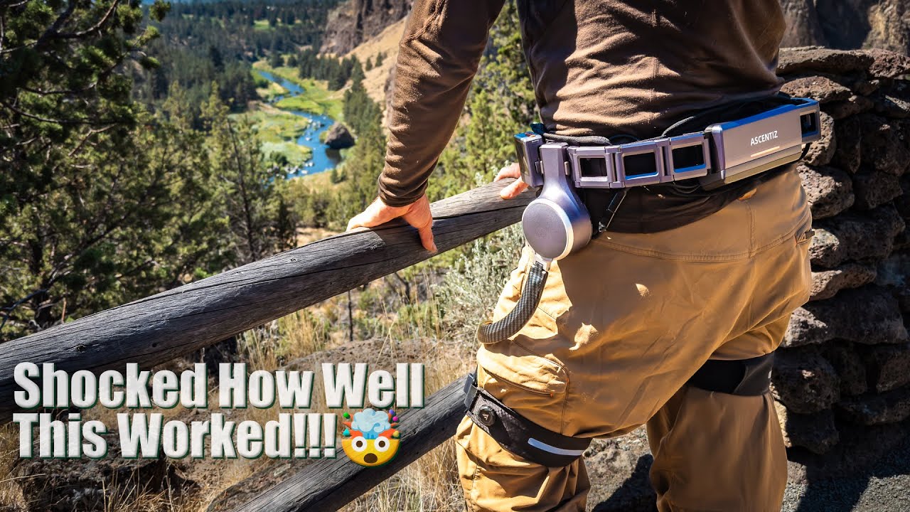 A man stands on mountain top to view the scene, wearing the Ascentiz hip-level exoskeleton.