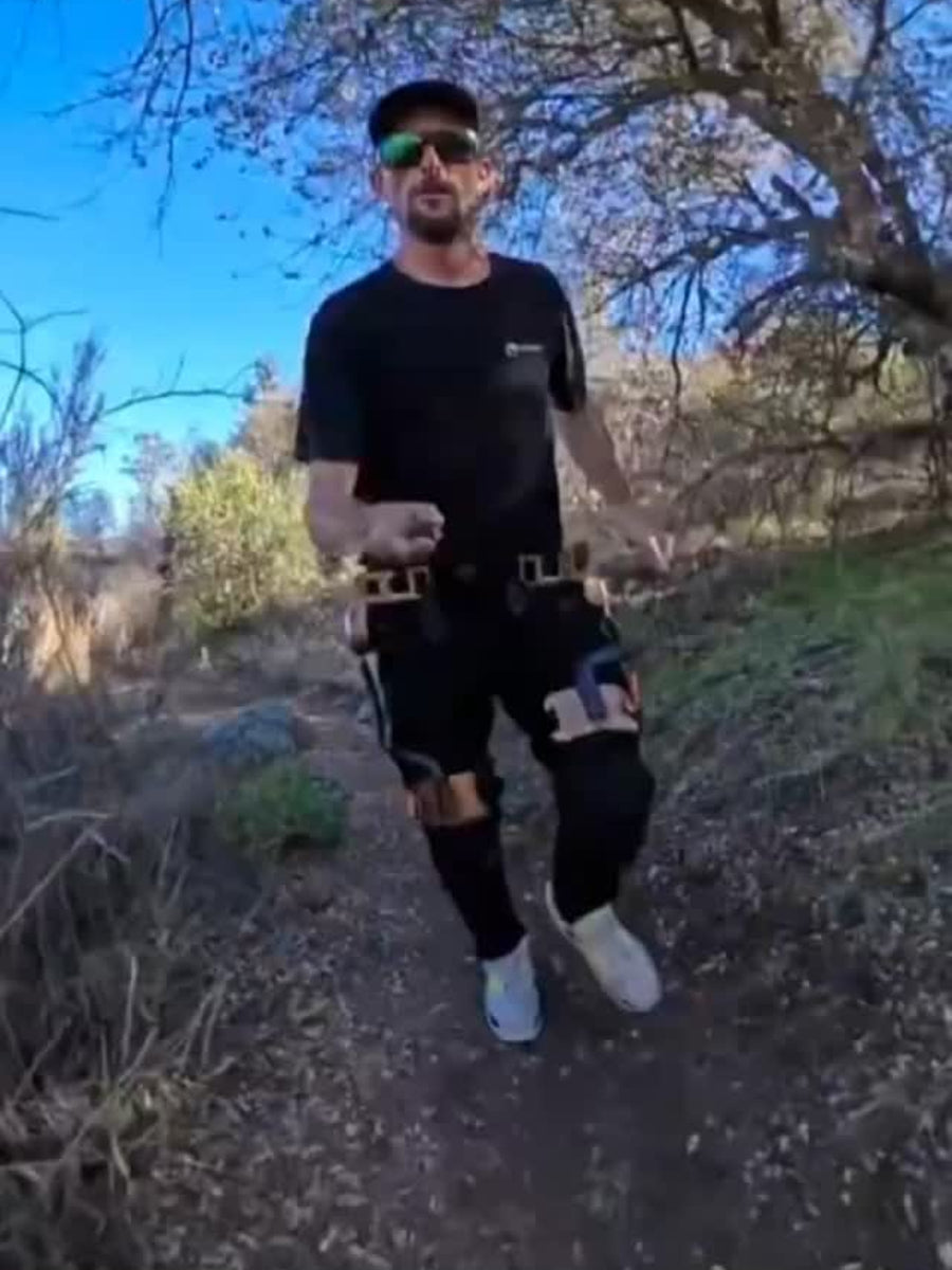 Action video cover of an outdoor hiker walking on a rugged trail, wearing the black Ascentiz modular hip exoskeleton. This wearable robotic hiking aid provides uphill hiking assistance to reduce leg fatigue and enhance physical endurance during long-distance treks.
