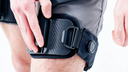 Close-up of a user adjusting the black textured thigh strap and mechanical dial on the Ascentiz WildFlex Kit for H Series exoskeleton.
