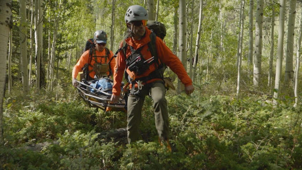 Two rescuers carrying a person in a wooded forest setting.
